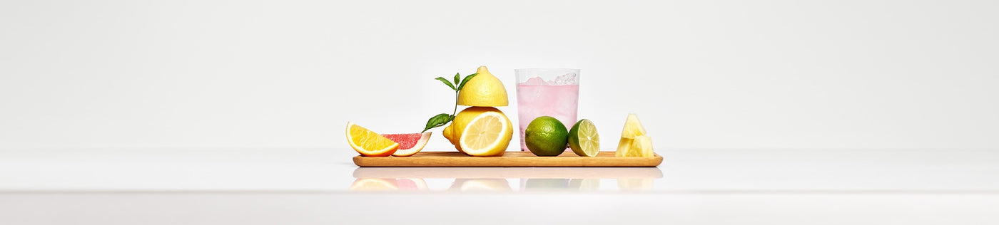 A glass of light-pink soda and a wooden board with cut-up citrus fruit