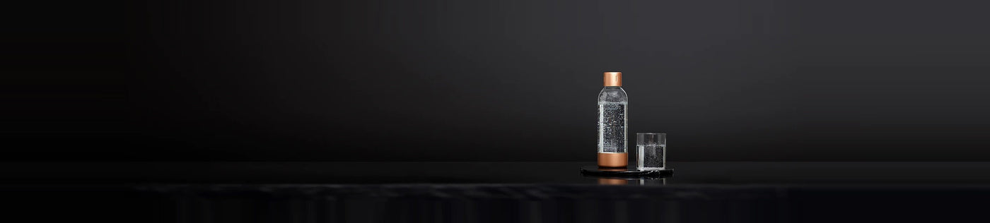 A Mysoda water bottle with copper lid and bottom and a glass of sparkling water in front of a black background