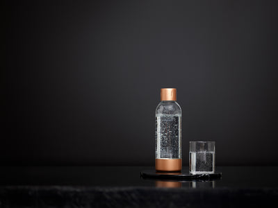 A copper Mysoda premium bottle and a glass of water in front of black background #väri_copper