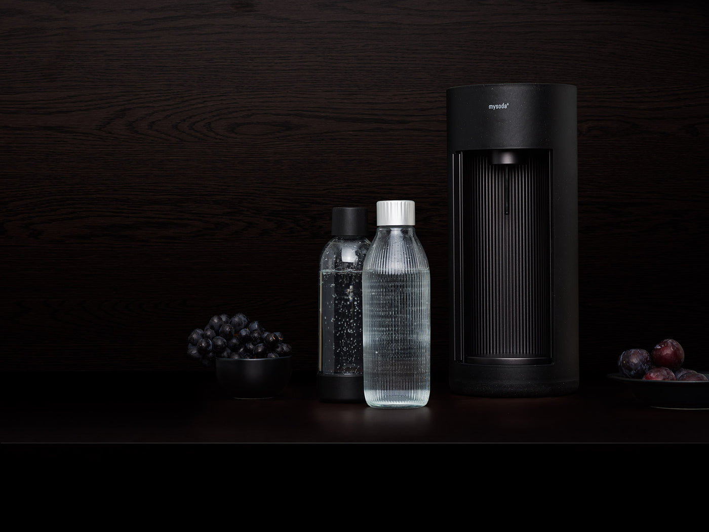 A black Glassy sparkling water maker and glass bottle in front of black background