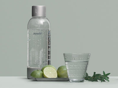 A silver premium bottle, fruit and a glass of water in front of pigeon background#väri_silver