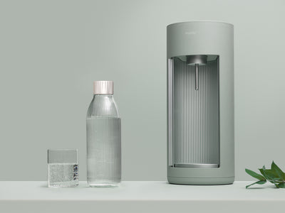 A pigeon-coloured Glassy sparkling water maker and glass bottle on tone-to-tone background