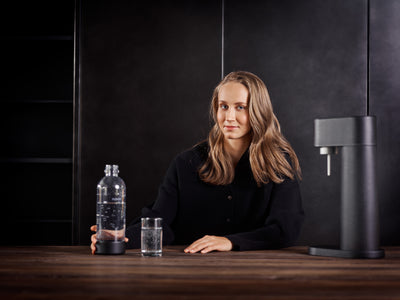Hurdler Viivi Lehikoinen enjoying a drink of sparkling water with Mysoda Woody. A black Woody sparkling water maker and respective PET water bottle are visible.